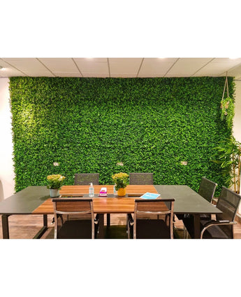 Une salle de réunion moderne comprend une longue table, des chaises noires, de petites plantes en pot, des cahiers et des bouteilles d'eau. Le mélange de tapis Kunsthaag 50x50 cm crée un fond luxuriant de murs verts et donne à la pièce un aspect frais et naturel.