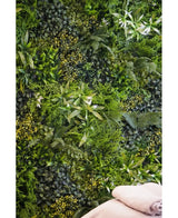 Une toile de fond luxuriante et texturée est créée par le mur de jardin vertical UV Kunsthaag Freshness 100x100 cm, densément recouvert de feuillage vert. Deux serviettes beiges pliées sont visibles en bas à droite.