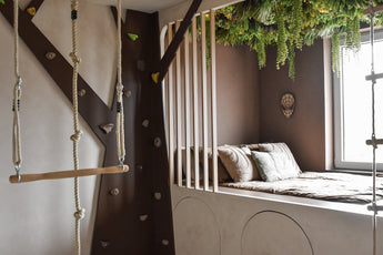 Une chambre d'enfant douillette avec un lit intégré et des oreillers est décorée avec la haie artificielle Lush Deco Deluxe 100x100 cm UV, qui ajoute une verdure luxuriante. Un mur d'escalade, une échelle de corde et une balançoire créent une sensation de cabane dans les arbres à la lumière du jour.