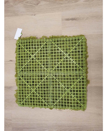 Le Artificial Haag Nordic Moss 50x50 cm UV est un tapis de gazon artificiel vert avec un dos en grille en plastique visible, idéal pour les intérieurs luxueux ou pour créer un mur végétal. Il repose sur un parquet en bois clair avec une petite étiquette blanche dans un coin.