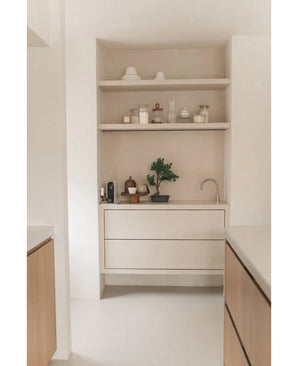 Coin cuisine minimaliste avec des étagères en bois clair avec des pots, des vases, de la décoration, un plan de travail avec du petit électroménager et la plante en pot Bonsaï Genévrier Artificiel de 40 cm, ainsi que des tiroirs intégrés et un petit robinet, le tout dans des tons neutres.