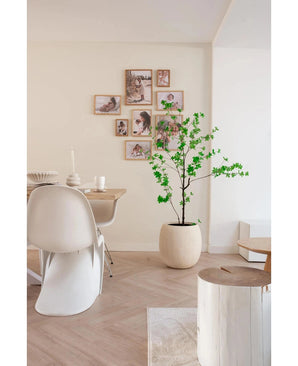 Une salle à manger moderne et minimaliste avec des chaises blanches, une table en bois et la plante artificielle Enkianthus de 150 cm qui ajoute de la verdure, complétée par une galerie murale de photos encadrées sur un fond de couleur neutre.