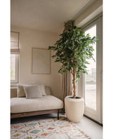 Un salon moderne avec un canapé beige, un coussin à rayures, une décoration murale abstraite, un tapis à motifs, une baie vitrée avec des rideaux transparents laissant entrer la lumière naturelle et une Plante Artificielle Ficus Vert 210 cm.