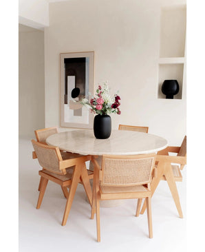 Een ronde marmeren tafel met vier houten stoelen omringt de Vaas Artic Black Ø21 x H29 cm gevuld met bloemen. Abstracte muurkunst en een zwart decorstuk op een ingebouwde plank maken de minimalistische, lichtgetinte kamer compleet.