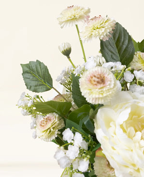 Een close-up van het Zijden kunstbloemen boeket White Love, met lichtgele en witte kunstbloemen met groene bladeren tegen een licht crèmekleurige achtergrond.