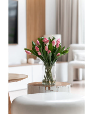 Het Zijden kunstboeket Tulpen in vaas Roze staat op een ronde witte houten tafel in een lichte, moderne woonkamer met neutrale tinten en een eigentijdse inrichting.