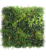 La haie artificielle Marisa 100x100 cm UV est un mur végétal carré et luxuriant avec des plantes à feuillage mixte, des fougères, des accents jaune-vert et des feuilles brunâtres éparses sur un fond blanc uni.