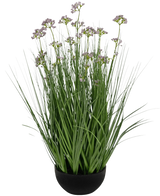 Le pot de gazon artificiel, fleur de poireau, oignon, ignifuge de 60 cm a de hautes et fines feuilles vertes ressemblant à de l'herbe et de délicates petites fleurs violettes dans un pot noir, sur un fond blanc.