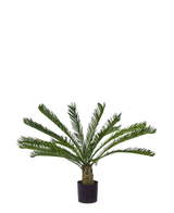 La plante artificielle Cycus Palm Deluxe 95 cm a des feuilles vertes plumeuses en surplomb et un tronc épais et structuré sur un fond blanc uni.
