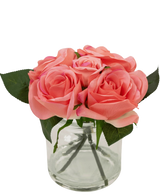 De Kunstrozenboeket Real Touch Roze 18cm heeft kleine roze kunstrozen met groene bladeren in een heldere glazen pot tegen een witte achtergrond.