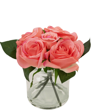 De Kunstrozenboeket Real Touch Roze 18cm heeft kleine roze kunstrozen met groene bladeren in een heldere glazen pot tegen een witte achtergrond.
